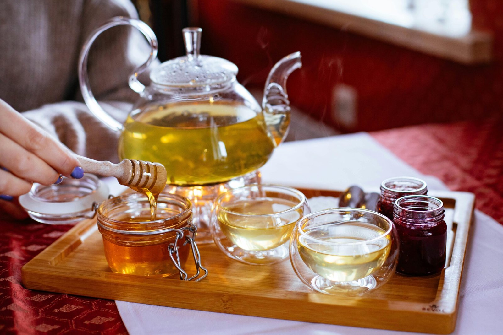 Stylish tea setup featuring honey, jam jars, and glass teapot in a warm indoor setting.